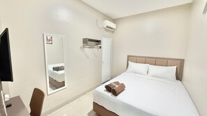 A hotel room with a bed, a chair, a mirror, a wardrobe, and an air conditioning unit. - New Kotjil Room (Jakarta)