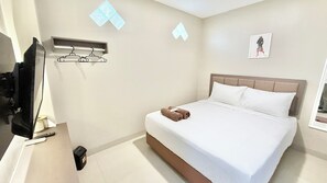 A hotel room with a bed, a TV, a wall-mounted light, and a small trash bin. - New Kotjil Room (Jakarta)