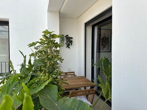 A balcony with a wooden table and chairs, surrounded by green plants. - Modern 1-bed Apartment in Val d’Anfa (Casablanca)