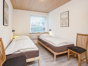 A small, cozy room with two wooden beds, a window with blinds, and a chair. - 6 Person Holiday Home in Gedser (Gedser)
