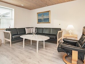 A living room with a black leather sofa, a white coffee table, and a wooden floor. - 6 Person Holiday Home in Gedser (Gedser)