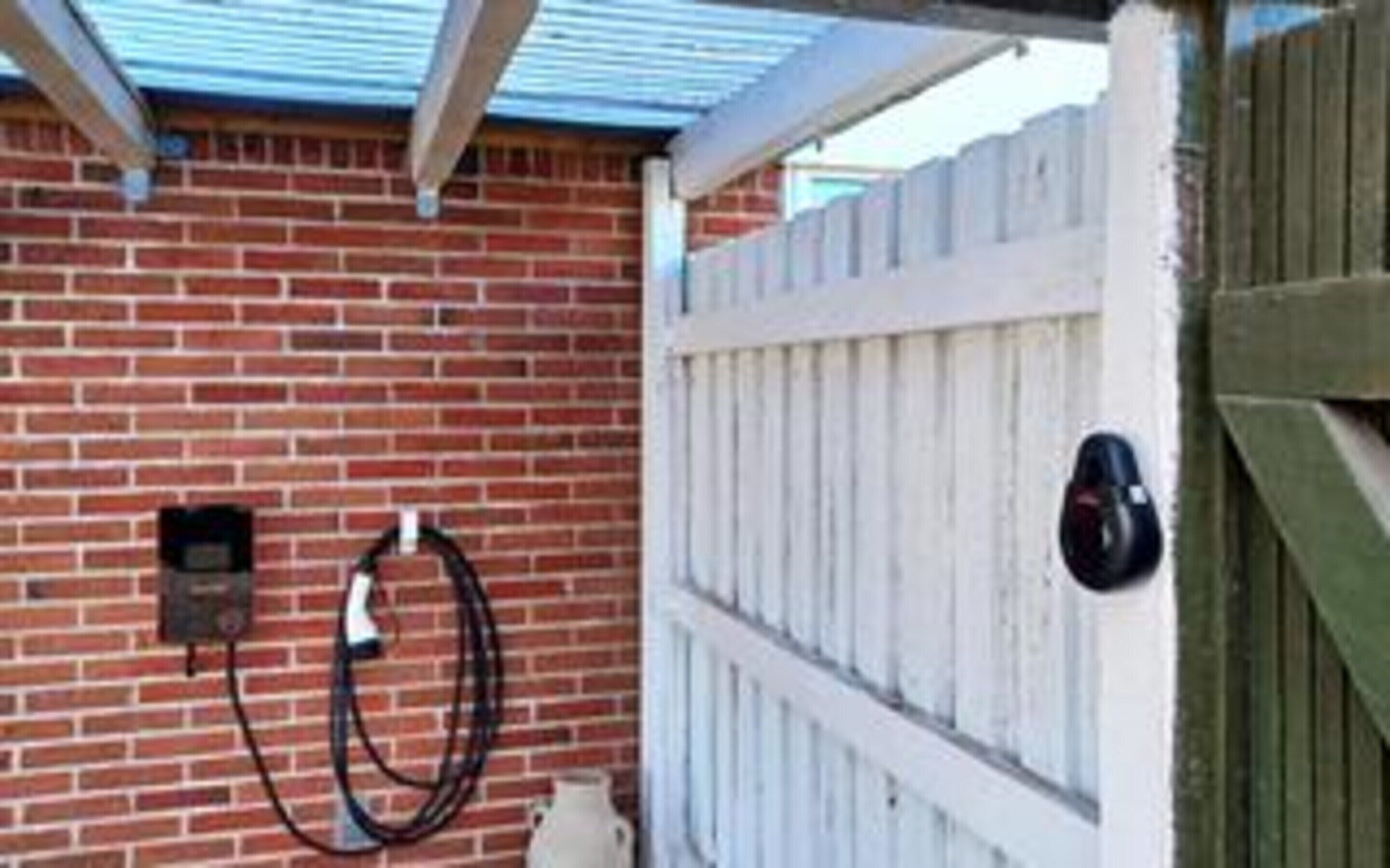 A brick wall with a white fence, a metal gate, and a hose attached to the wall.