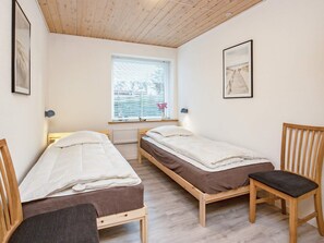 A room with two wooden beds, a window with blinds, a chair, and a framed picture on the wall. - 6 Person Holiday Home in Gedser (Gedser)
