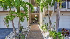 A pathway leading to a building with numbered garage doors, surrounded by palm trees and plants. - Newly Updated, Walk to Siesta Key Beach, Tennis, Heated Pool (Siesta Key)