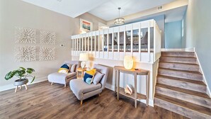A modern living room with a staircase, wooden flooring, two grey armchairs, a side table, and decorative wall art. - Newly Updated, Walk to Siesta Key Beach, Tennis, Heated Pool (Siesta Key)