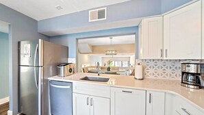 A modern kitchen with white cabinets, a stainless steel refrigerator, a coffee maker, and a built-in dishwasher. - Newly Updated, Walk to Siesta Key Beach, Tennis, Heated Pool (Siesta Key)