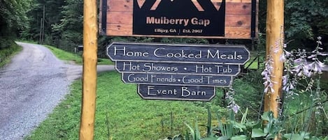 A wooden sign with a mountain logo and text for Mulberry Gap, listing amenities like home-cooked meals, hot showers, and a barn.