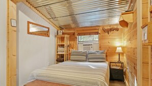 Ein gemütliches Schlafzimmer in einer Holzhütte mit Bett, einer Bank, einem Nachttisch mit Lampe und einem Fenster.