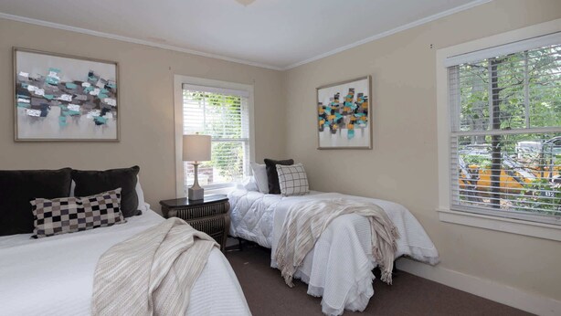 A bedroom with two beds, a nightstand, a lamp, and abstract art on the walls.