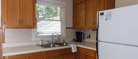 A kitchen with wooden cabinets, a white refrigerator, a window with blinds, and a tiled floor.