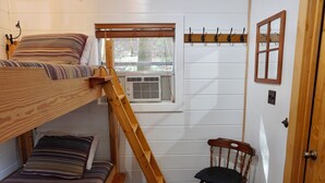 Una cama litera con escalera, una silla, una ventana con persianas y un perchero.