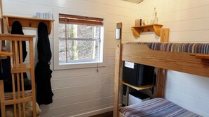 Dormitorio con literas, ventana, estanterías de madera y una mesita.