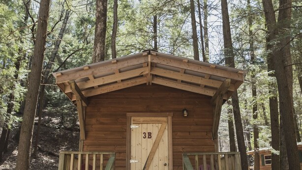 Una cabaña de madera con una puerta que indica "3B" en un área boscosa.