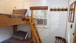 Habitación con literas, una escalera de madera, una ventana con persianas, un perchero en la pared y una silla.