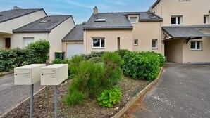 Une rangée de maisons modernes à deux étages, avec une allée pavée et un petit jardin agrémenté d’arbustes et d’une plante en pot.