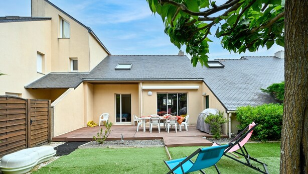 Un jardin avec une terrasse, une table et des chaises, une chaise bleue et un arbre.