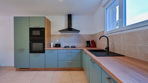 Una cocina moderna con gabinetes verde azulado, una campana extractora negra, un fregadero y una ventana que proporciona luz natural.