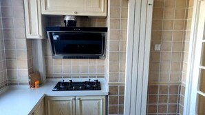 Une cuisine compacte dotée d’un four à micro-ondes encastré, d’une cuisinière et d’un meuble blanc.