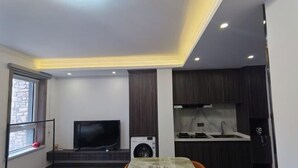 Un espace de vie compact comprenant un coin repas, un téléviseur, un lave-linge et une kitchenette.
