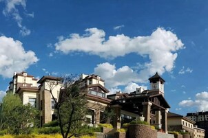 Un edificio de varios pisos con una torre destacada, rodeado de vegetación y bajo un cielo despejado.