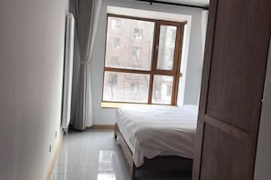 Un dormitorio con un ventanal grande, una cama y un armario de madera.