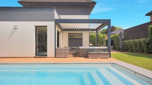 Ein modernes Haus mit Swimmingpool, Sitzgelegenheiten im Freien und einer überdachten Terrasse.
