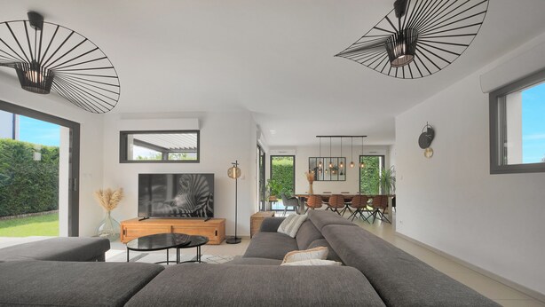 Ein modernes Wohnzimmer mit einem großen Ecksofa, einem Flachbildfernseher und einem Essbereich mit Tisch und Stühlen.