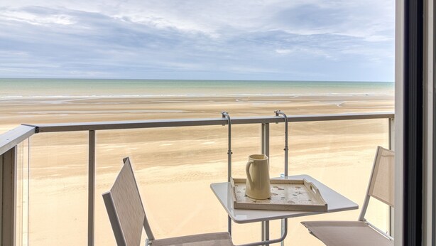 Un balcón con vista a la playa, una mesa con una jofaina y una bandeja, y dos sillas.