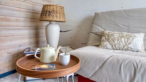 Un dormitorio acogedor con un cabecero de madera, una mesita de noche redonda con una lámpara, un hervidor y una taza.