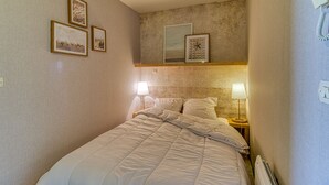 Una habitación de hotel con una cama, dos lámparas de noche, un reloj de pared y tres cuadros enmarcados.