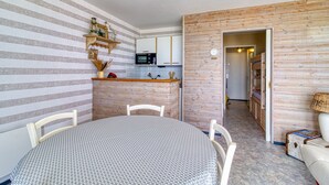 Una cocina compacta con microondas, un refrigerador pequeño y un mueble de madera. Hay una mesa de comedor con sillas y un pequeño sofá en la sala de estar.