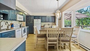 A modern kitchen with dark blue cabinets, a white microwave, and a dining area with wooden chairs and a table. - Waterfront Hot Tub Retreat w Kayaks | Kayak Point (North Fork)