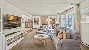 A spacious living room with a large flat-screen TV, comfortable seating, bookshelves, and a stone fireplace. - Waterfront Hot Tub Retreat w Kayaks | Kayak Point (North Fork)