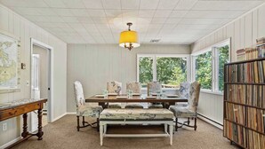 A dining area with a wooden table, patterned chairs, a bench, and a bookshelf. - Waterfront Hot Tub Retreat w Kayaks | Kayak Point (North Fork)