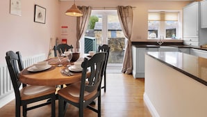 Un comedor con mesa y sillas de madera, una cocina con pileta y muebles, y vista a través de un vidrio.