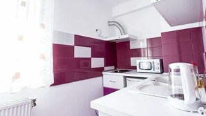 A modern kitchen with white cabinets, a microwave, a kettle, and a window with sheer curtains. - Luxorvilla studios (Constanta)