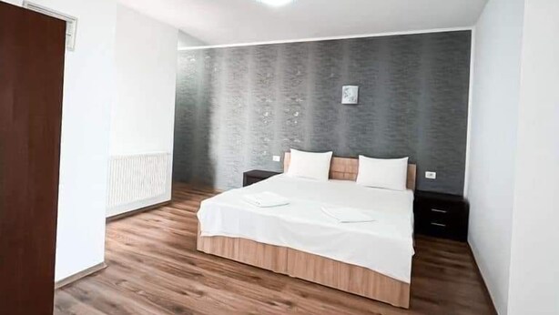 A bedroom with a wooden floor, a bed with white bedding, a nightstand, and a wall-mounted radiator. - Luxorvilla studios (Constanta)