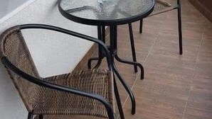 A balcony with wicker chairs and a glass table, a window, and a view of buildings. - Luxorvilla studios (Constanta)