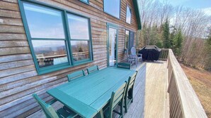 A wooden deck with a green table and chairs, a barbecue grill, and a view of the surrounding forest. - Mountain View Escape - Stunning Views! Bethlehem, NH Cabin Near Skiing & Hiking (Bethlehem)