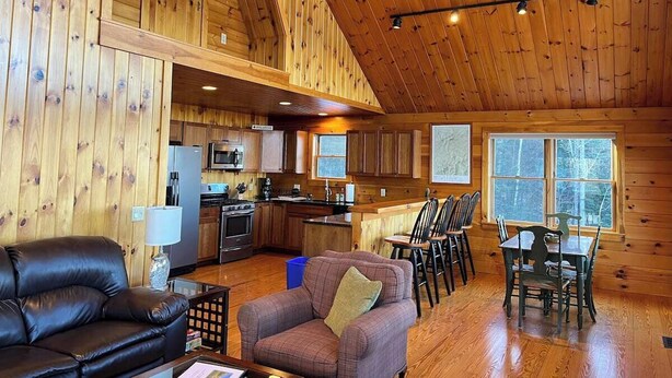 A cozy cabin interior with a living room, dining area, kitchen, and a large window. - Mountain View Escape - Stunning Views! Bethlehem, NH Cabin Near Skiing & Hiking (Bethlehem)