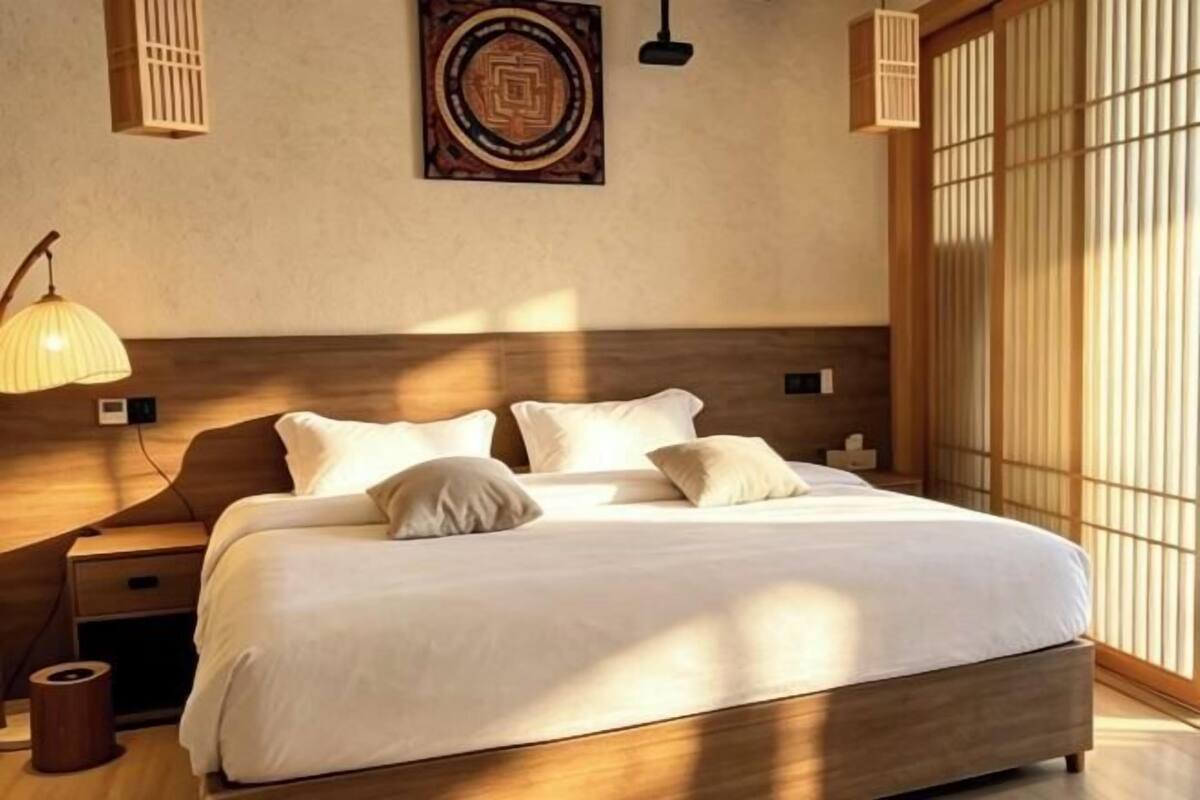Una cama bien hecha con cabecera de madera, lámpara de noche y una obra de arte colgada en la pared.