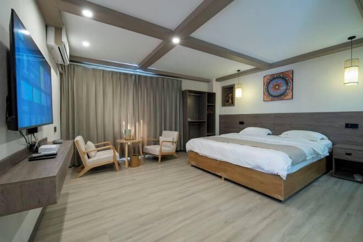 Una habitación de hotel moderna con cama, dos sillas, escritorio, televisor y armario.