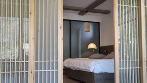 Une pièce comprenant un lit, une lampe suspendue et une porte coulissante avec des stores verticaux.