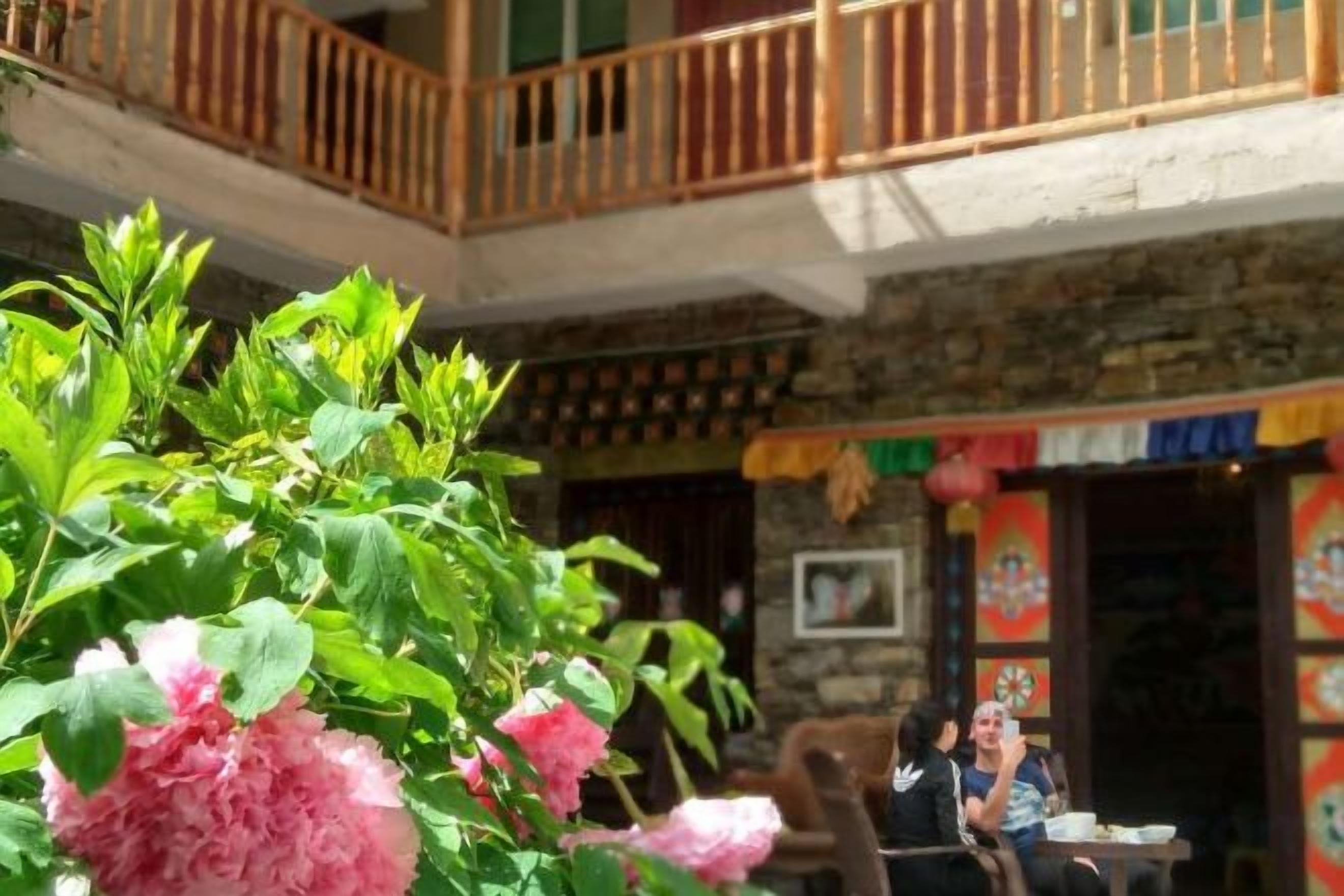 A courtyard with a stone building, wooden balcony, and a person sitting at a table.