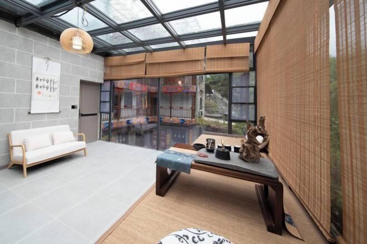 Un interior moderno con techo de vidrio, un sofá blanco, una mesa de madera con objetos decorativos y vistas amplias por grandes ventanas.