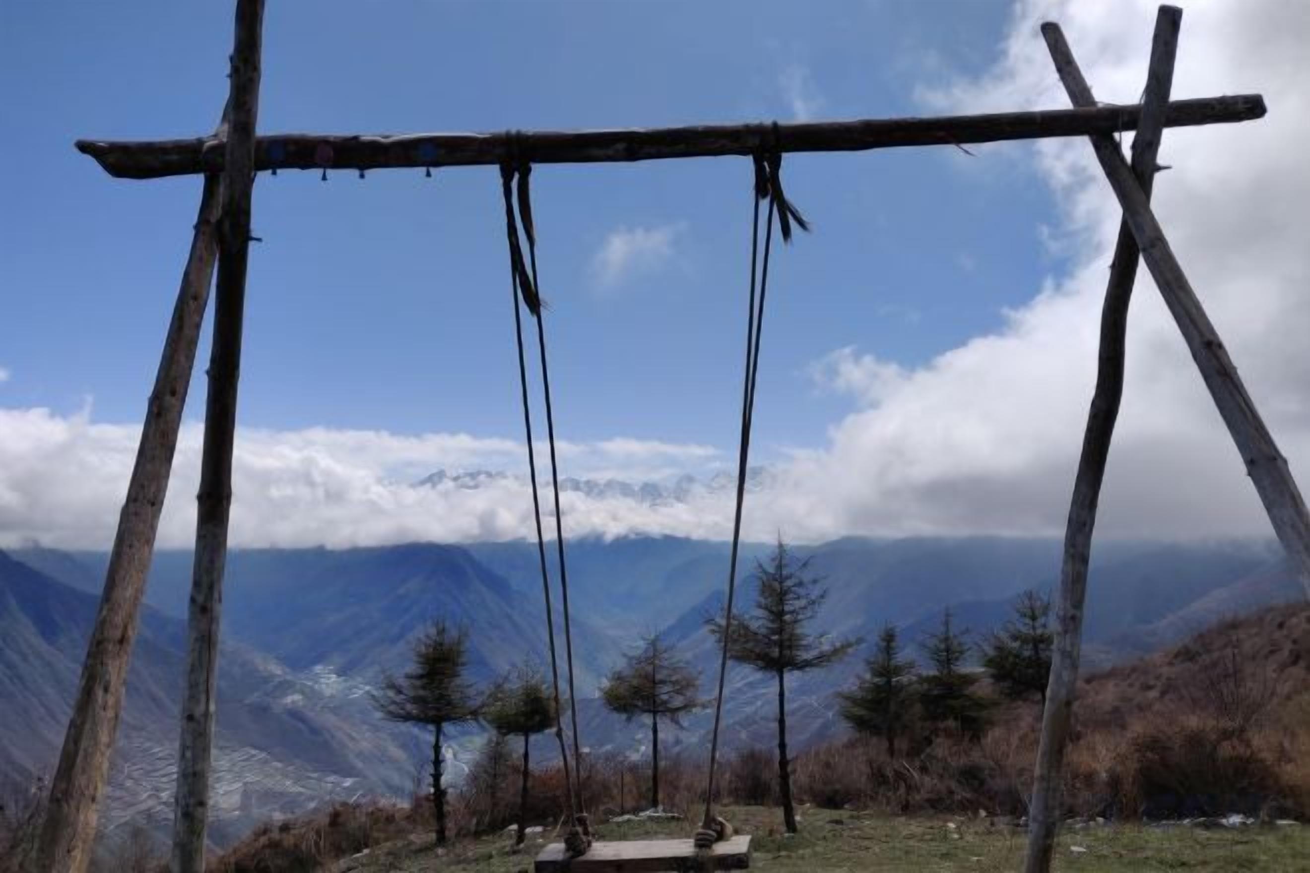 A wooden swing set in a mountainous area with a clear sky.