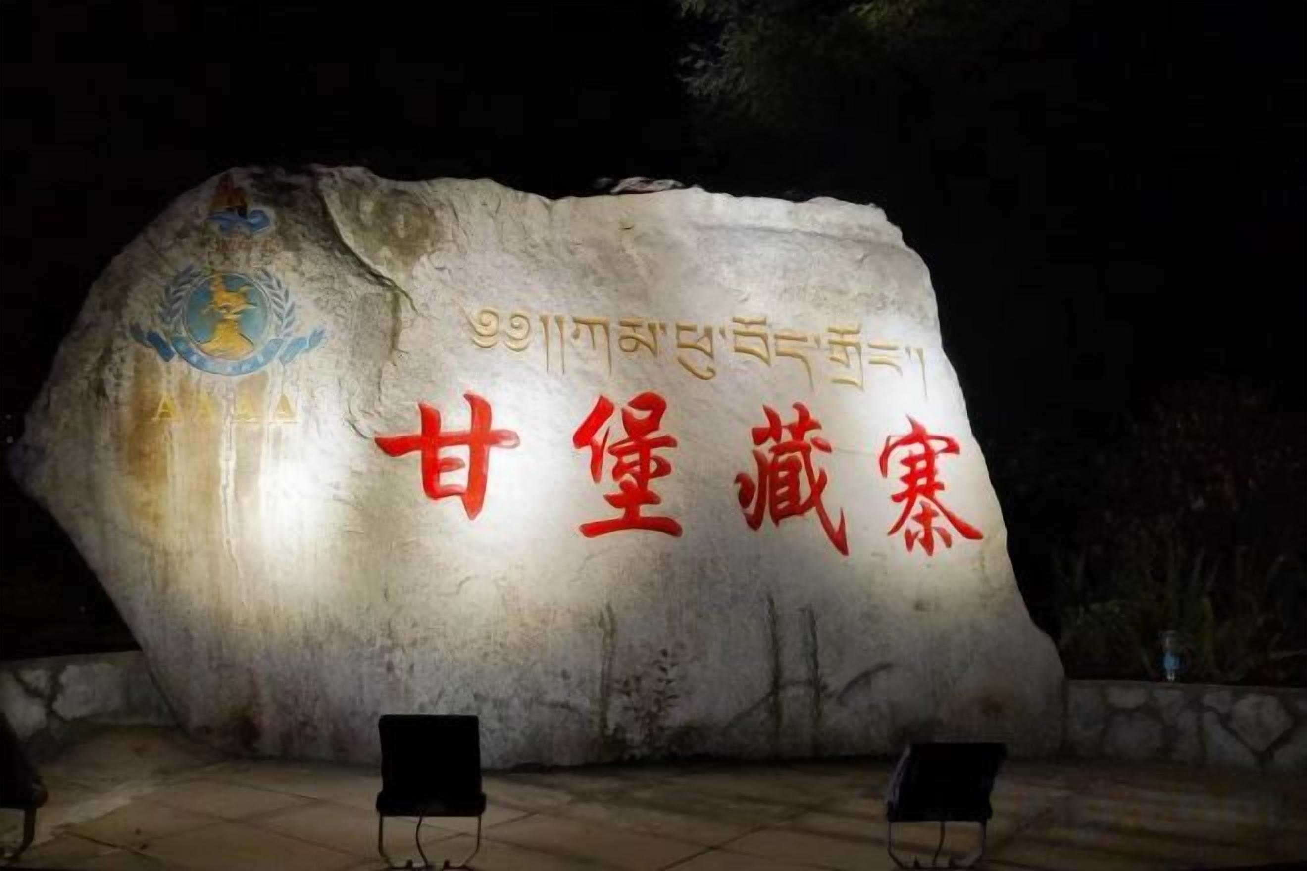 Un gran monumento de piedra con inscripciones y un logotipo, rodeado de una zona pavimentada con dos sillas.