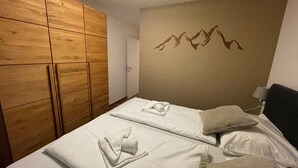 A hotel room with a wooden wardrobe, a bed with neatly folded towels, and a wall with a mountain design. - Residence Alpin TOP 6 - Kaprun incl SUMMER CARD (Kaprun)