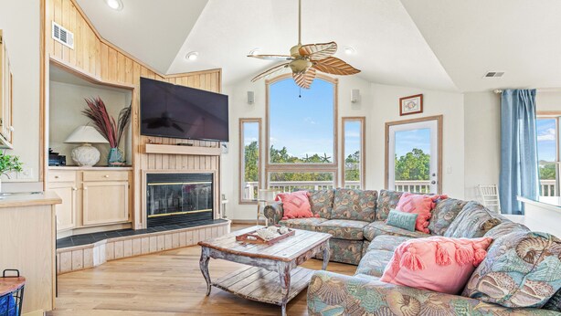 A spacious living room with a fireplace, large windows, and a ceiling fan. - Spacious Pet Friendly 6-bedroom all season retreat in Corolla w/ pool and sauna (Corolla)