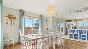 A spacious dining area with a large table and chairs, a chandelier, and a view of the beach. - Spacious Pet Friendly 6-bedroom all season retreat in Corolla w/ pool and sauna (Corolla)